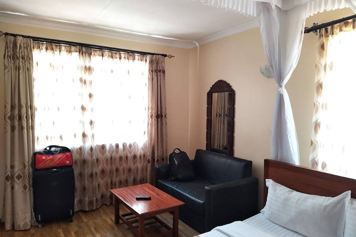 A hotel room with a bed, a wooden table, a black sofa, and a large mirror.