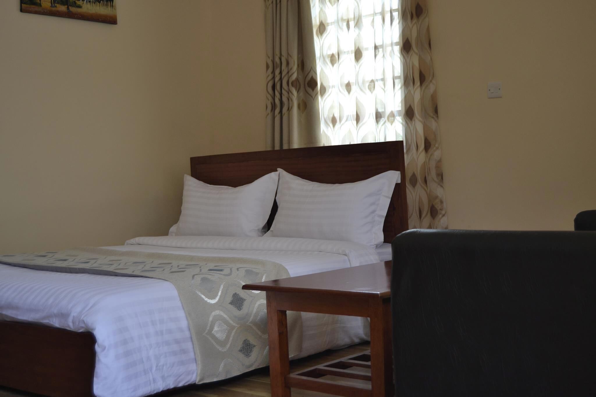 A neatly made bed with white linens, a wooden headboard, and a small wooden table beside it.