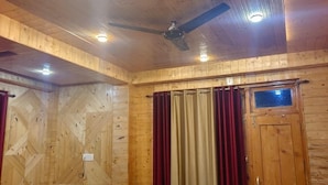 Um quarto com painéis de madeira, uma cama, um ventilador de teto e uma janela com cortinas.