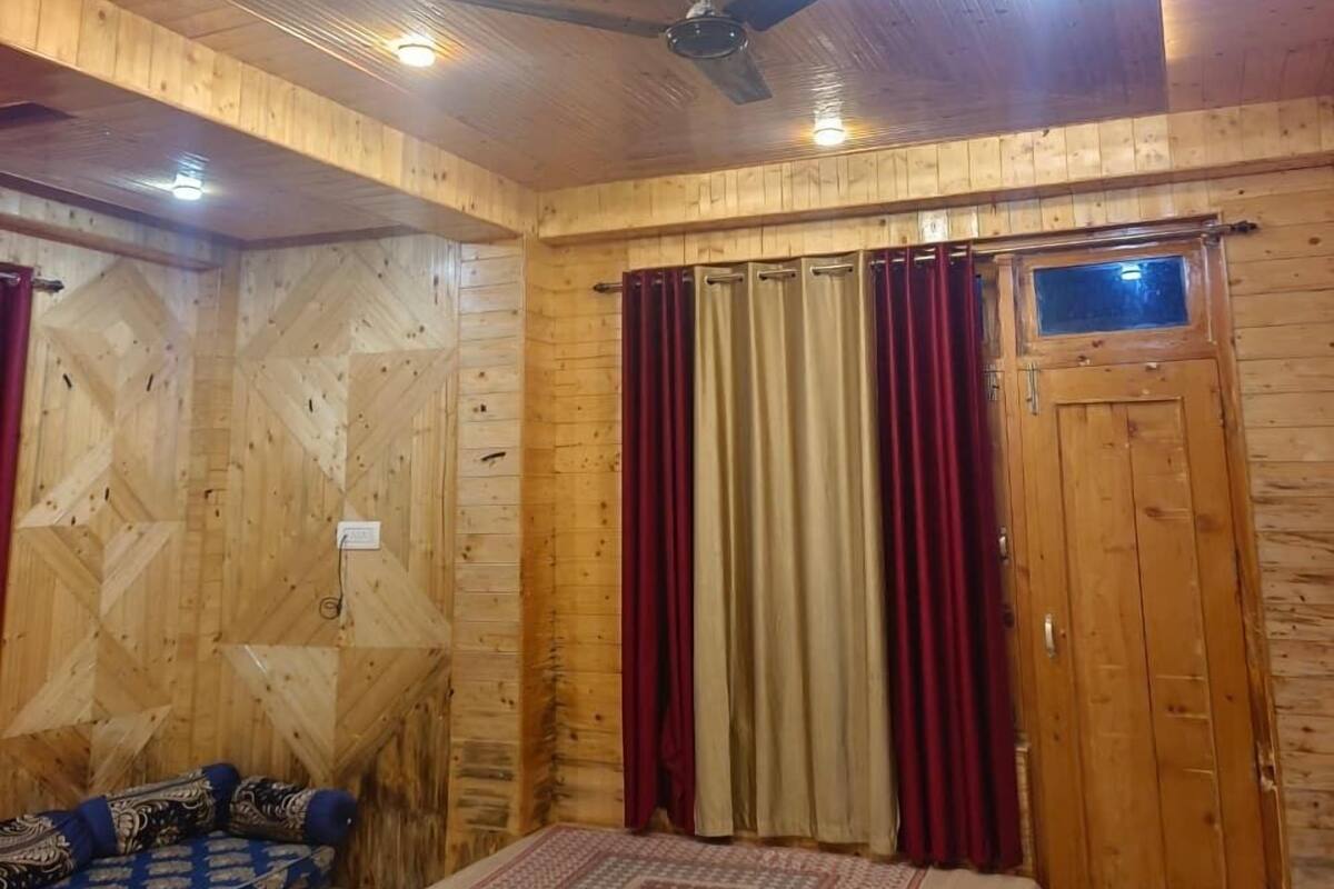 Una habitación con paneles de madera, una cama, un ventilador de techo y una ventana con cortinas.