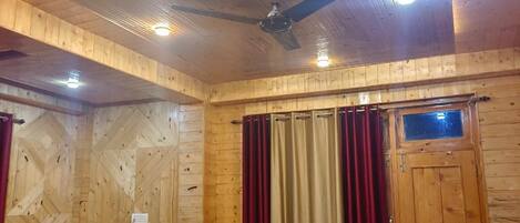 Una habitación con paneles de madera, una cama, un ventilador de techo y una ventana con cortinas.