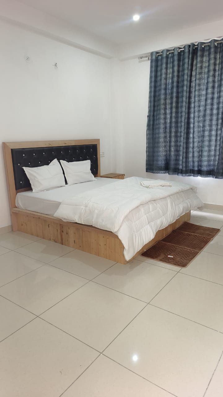 Un dormitorio con estructura de cama de madera, ropa de cama blanca y una ventana con cortinas azules.