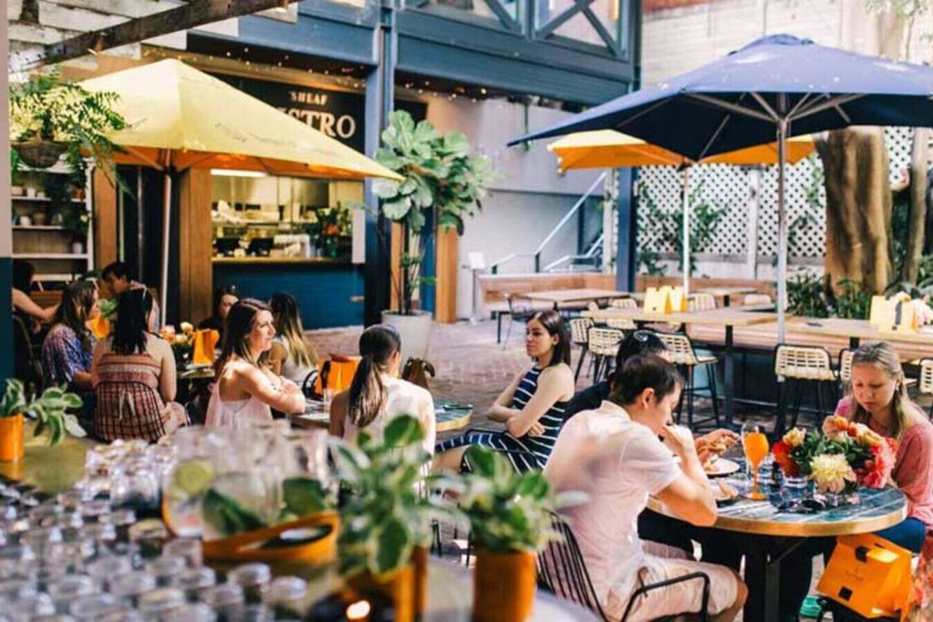 An outdoor dining area with tables and chairs, umbrellas, and potted plants.