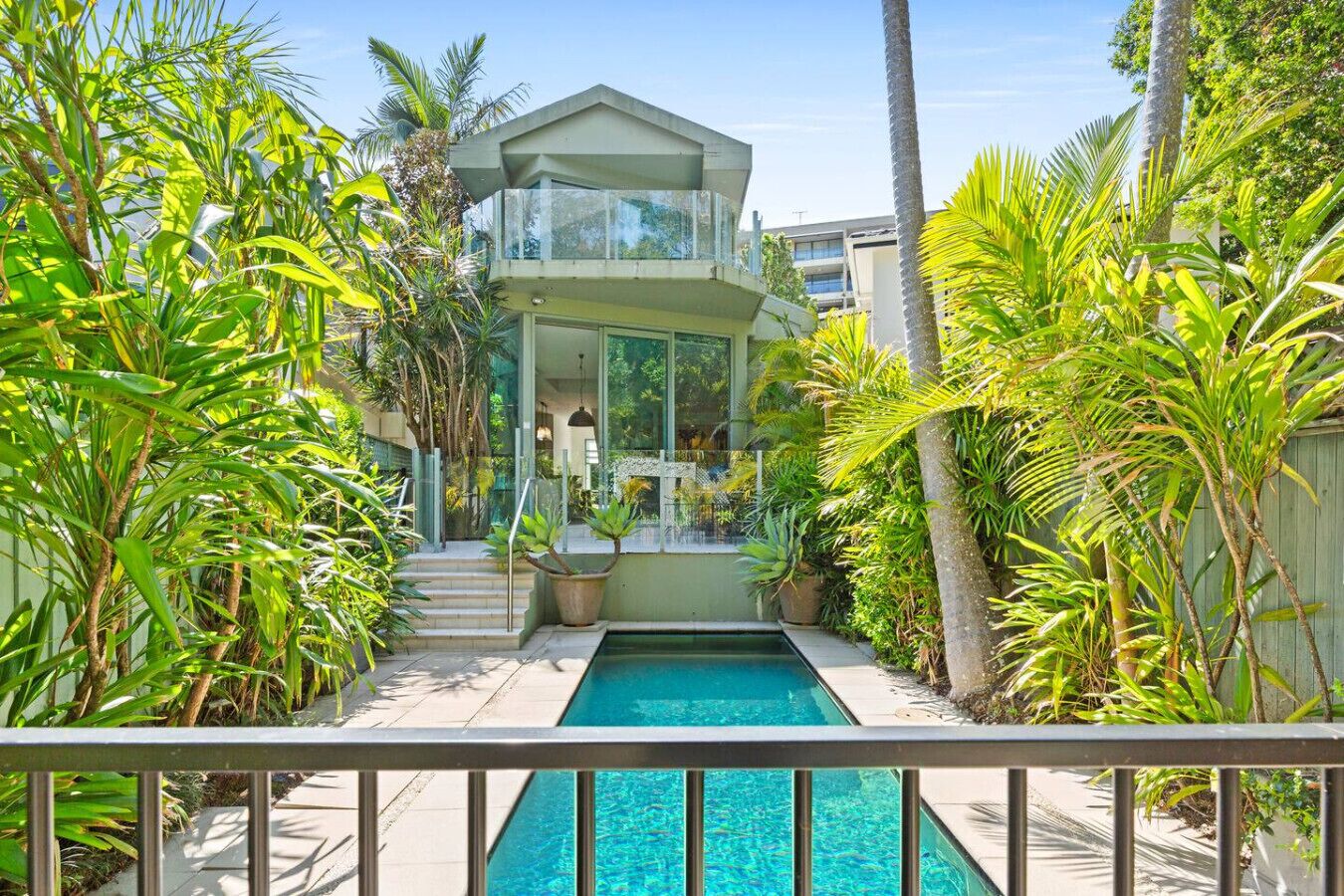 A modern two-story house with a swimming pool, surrounded by tropical plants.
