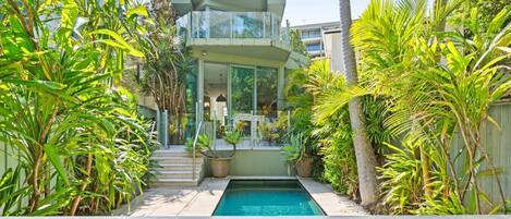 A modern two-story house with a swimming pool, surrounded by tropical plants.