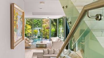 A modern living room with a glass staircase, a painting on the wall, and a view of the outdoors.