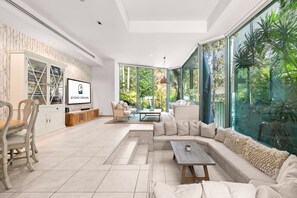 Una sala de estar moderna con un sofá modular, una mesa de centro y un televisor. Hay un ventanal con vistas a zonas verdes.