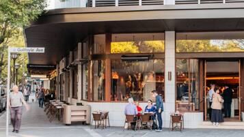An outdoor cafe area with tables and chairs, a covered seating area, and a building entrance.