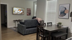 Un salon moderne avec un canapé gris, une table à manger avec des chaises et un coin cuisine doté de plans de travail en granit.