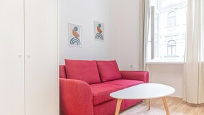 Un canapé rouge et une table blanche se trouvent dans une pièce dont le sol est en bois, les murs sont blancs, et où l’on peut admirer deux œuvres d’art abstrait accrochées au mur.