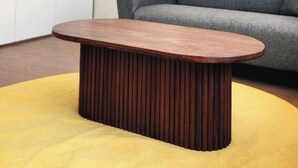 Een moderne woonkamer met een grijze bank, een houten salontafel en een geel vloerkleed.