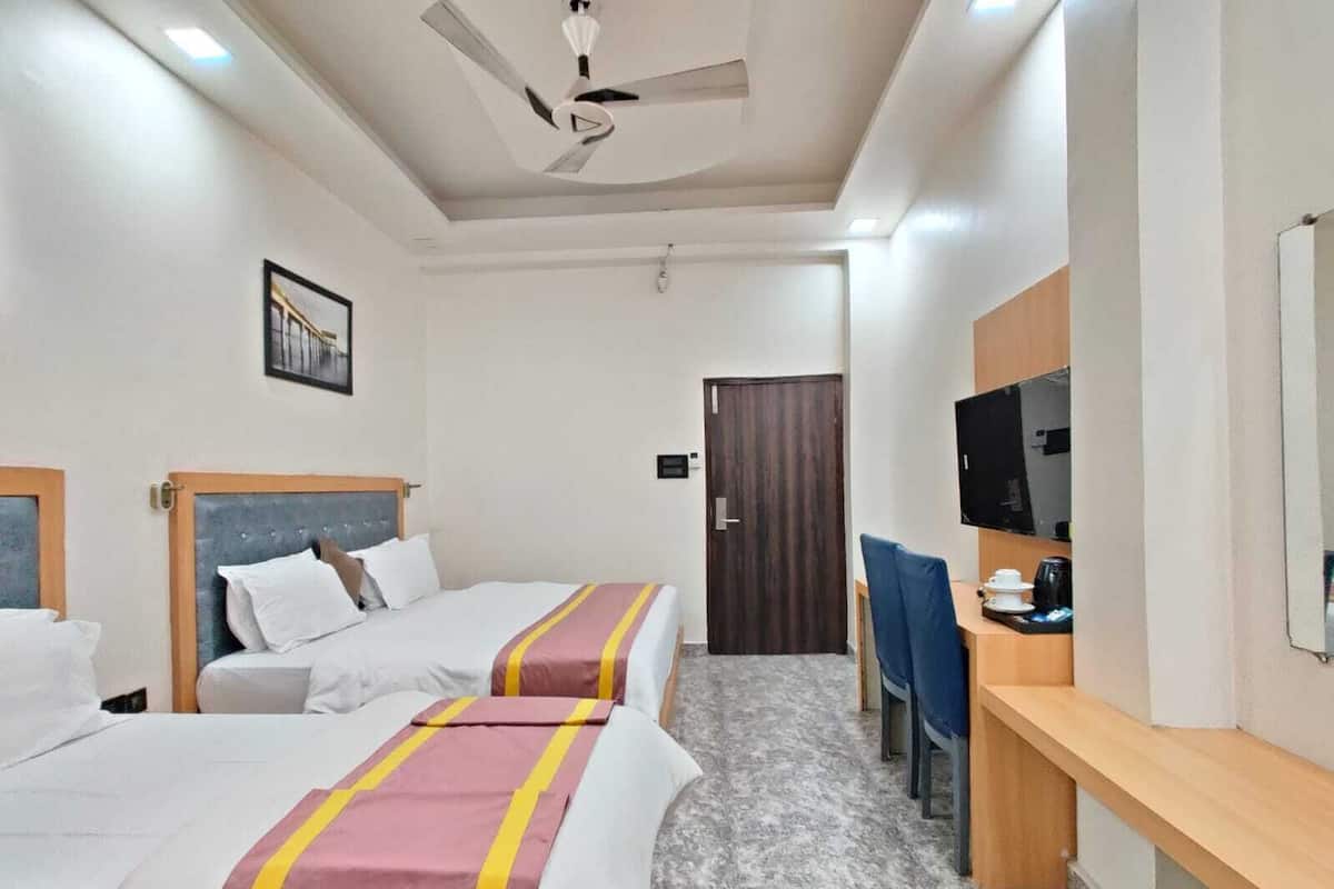 A hotel room with two beds, a desk with a chair, a television, and a ceiling fan.