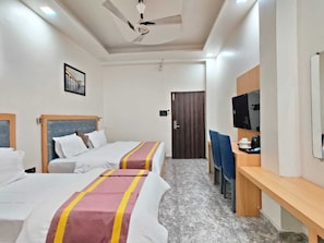 A hotel room with two beds, a desk with a chair, a television, and a ceiling fan. - GOLDEN GSC HOTEL (Amritsar)