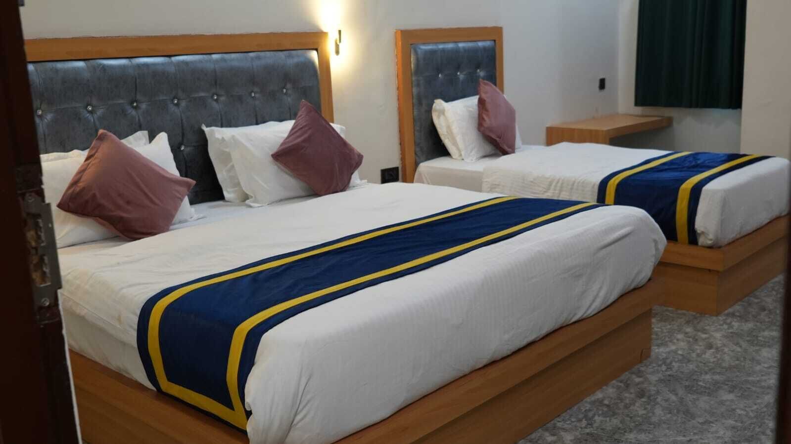 A hotel room with two beds, each with a headboard, white bedding, and a blue and yellow striped blanket.
