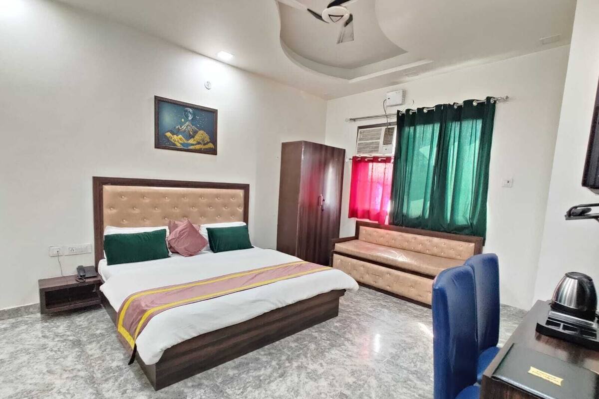 A hotel room with a bed, a desk, a chair, a wardrobe, and a painting on the wall.