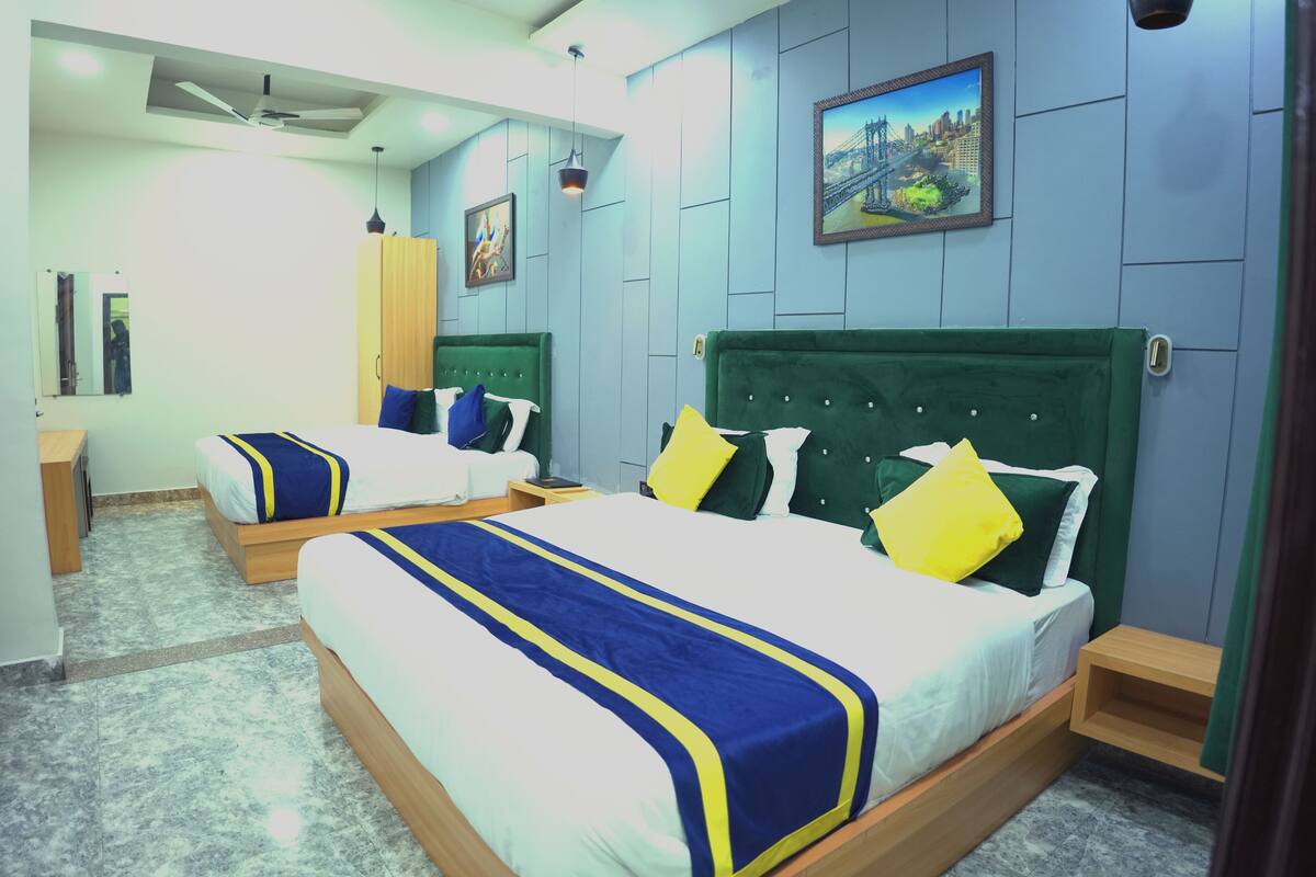 A hotel room with two beds, each with a green headboard and white bedding. There are wooden nightstands, a ceiling fan, and a painting on the wall.