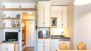 A compact kitchen with white cabinets, a wooden dining table, and a TV. - Cosy Mountain Retreat for 4 Guests (Villard-de-Lans)