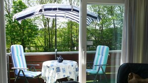 A balcony with two striped chairs, a table with a blue and white tablecloth, and a large umbrella. - Ferienwohnung in St. Peter-ording (St. Peter-Ording)