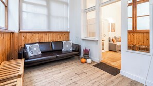 A modern living room with a black leather sofa, wooden paneling, and large windows. - Imperial Apartments - Nadmorski Park (Sopot)