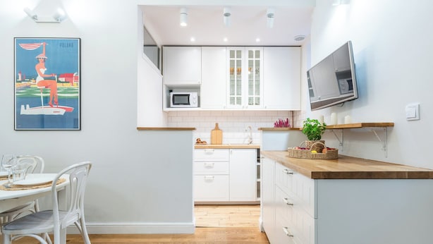 A modern kitchen with white cabinets, a microwave, and a wooden countertop. There is a dining area with white chairs and a table. - Imperial Apartments - Nadmorski Park (Sopot)