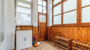 A room with wooden walls, large windows, a white cabinet, a ladder, a small pumpkin, and a wicker basket with flowers. - Imperial Apartments - Nadmorski Park (Sopot)