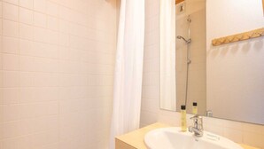 A bathroom with white tiled walls, a wooden vanity with a sink, and a shower area with a glass door. - Mountain Hideaway in Risoul (Risoul)