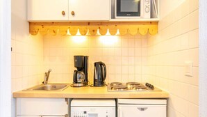A compact kitchen with white cabinets, a microwave, a coffee maker, a kettle, a stove, and a dishwasher. - Mountain Hideaway in Risoul (Risoul)