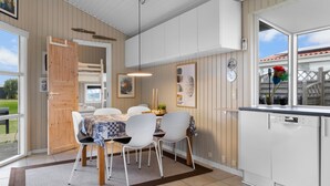 Een moderne keuken met witte kastjes, een eethoek met tafel en stoelen, en een groot raam met uitzicht.