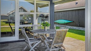 Een overdekt buitengebied met een houten terras, een tafel met stoelen en een groene parasol.