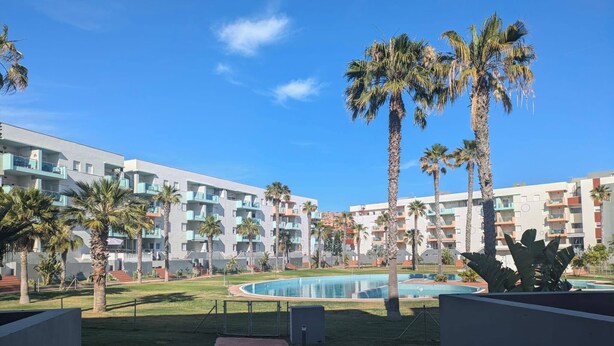 Een resort met meerlaags gebouwen, palmbomen en een zwembad.