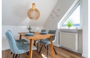 Un coin repas comprenant une table en bois, quatre chaises, un luminaire suspendu, une fenêtre donnant sur un paysage et un radiateur.