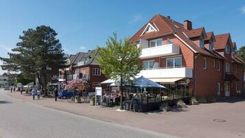 Eine Straße mit einer Reihe roter Backsteingebäude, ein Fußgängerbereich mit Außenbestuhlung und einem strahlend blauen Himmel.