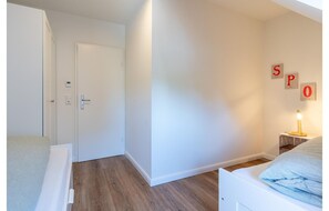 Ein Schlafzimmer mit einem Bett, einem Nachttisch, einer Wandlampe und einer Tür zu einem anderen Raum.