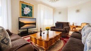 A living room with a large flat-screen TV, a wooden coffee table, brown sofas, and a red carpet.