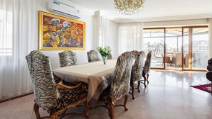 A dining area with a large table, zebra-patterned chairs, a chandelier, and a colorful painting on the wall.