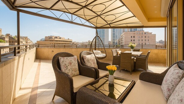 A rooftop terrace with wicker furniture, a hanging chair, and a glass table with yellow flowers.