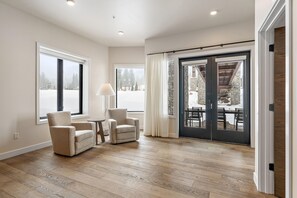 Una habitación amplia con un gran ventanal corredizo que da a un espacio exterior con un muro de piedra y una terraza de madera.