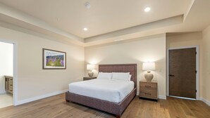 Une chambre à coucher avec un grand lit, deux tables de chevet avec des lampes, une porte et un tableau encadré au mur.