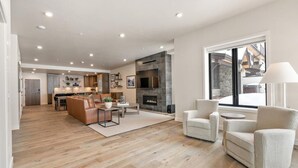 A spacious living area with a fireplace, a dining area, and a kitchen visible through an open door. - Slopeside Sanctuary|Exclusive Tamarack Perks (Tamarack)