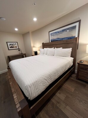 Una habitación de hotel con una cama grande, cabecera de madera, una mesita de noche, una lámpara y un cuadro en la pared.