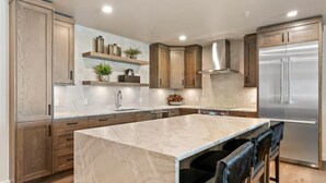A modern kitchen with wooden cabinets, a marble island, and stainless steel appliances. - Slopeside Sanctuary|Exclusive Tamarack Perks (Tamarack)
