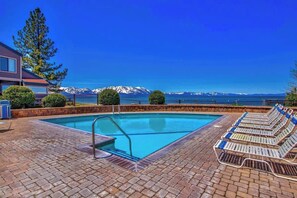 Ein Schwimmbad mit Blick auf Berge, Liegestühlen und einer Ziegelterrasse.