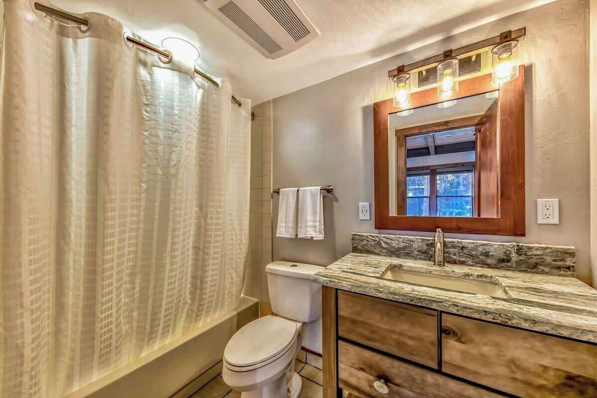 Een badkamer met douchegordijn, toilet, wastafel en wastafelmeubel.