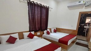 A hotel room with two beds, each with white bedding and red accents, a ceiling fan, an air conditioning unit, and a bathroom visible through a doorway.