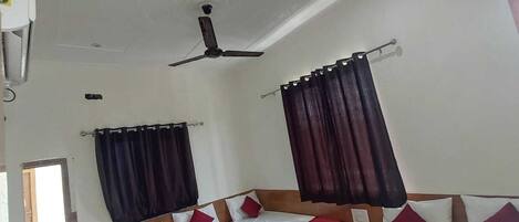 A hotel room with two beds, dark curtains, a ceiling fan, and a window.