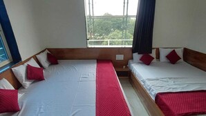 A room with two beds, each with white linens and red accents, a window with a view of greenery, and a curtain.