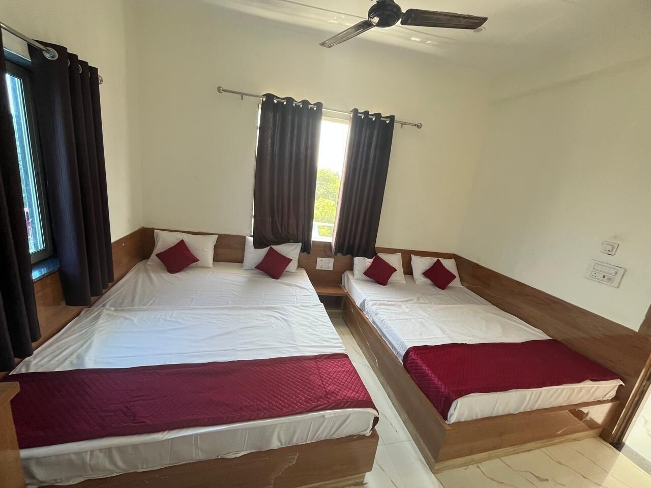 A room with two beds, each with white bedding and red pillows, a ceiling fan, and a window with curtains.