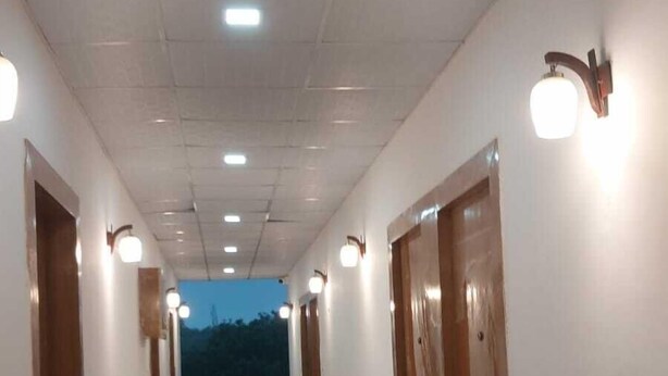 A long, well-lit hallway with tiled floors and wooden doors, leading to a balcony with a view of the sky.
