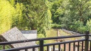 A deck with a table and chairs overlooking a natural landscape with trees and a body of water. - Le Moulin de Cambelong (Conques-en-Rouergue)