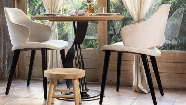 A dining area with two chairs and a small table, large windows with curtains, and a view of greenery outside.